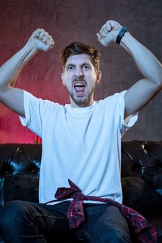 Young supporter man watching football game on television sitting at home couch with beer and chips in stress dejected and disappointed for failure shouting and complaining.