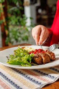 Eating grilled pork kebab with red bell pepper and green salad in a restaurant