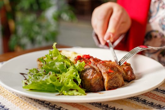 Eating grilled pork kebab with red bell pepper and green salad in a restaurant