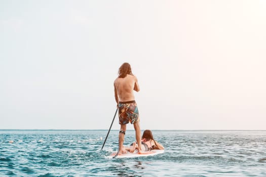 Silhouette of woman standing, surfing on SUP board, confident paddling through water surface. Idyllic sunset or sunrise. Sports active lifestyle at sea or river.