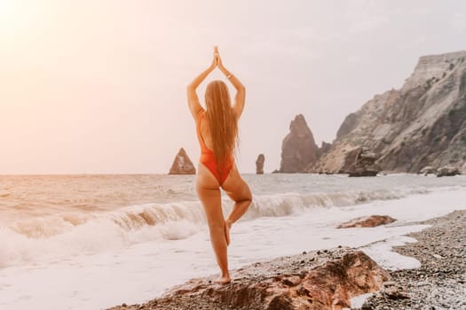 Woman sea yoga. Back view of free calm happy satisfied woman with long hair standing on top rock with yoga position against of sky by the sea. Healthy lifestyle outdoors in nature, fitness concept