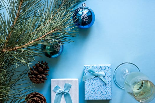 New Year's still life - a glass of champagne, Christmas decorations and spruce branches on blue background. Top view. Copy space. Flat lay