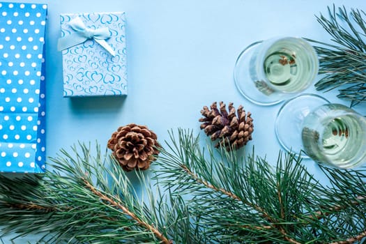 New Year's holiday with spruce branches, Christmas presents and with a pair of wine glasses of champagne on blue background. Flat lay, top view, copy space
