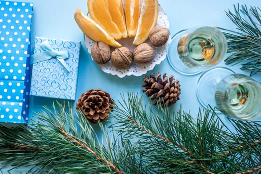 New Year's holiday with spruce branches, Christmas presents and with a pair of wine glasses of champagne on blue background. Flat lay, top view, copy space