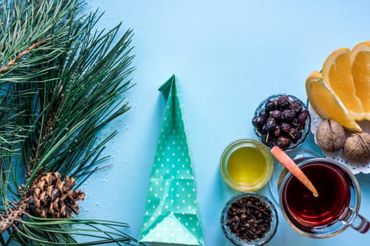Hot mulled wine with orange, anise, cardamon and cinnamon on blue background. Christmas tree branches, gifts and cones. Flat lay, copy space, top view. Holidays.