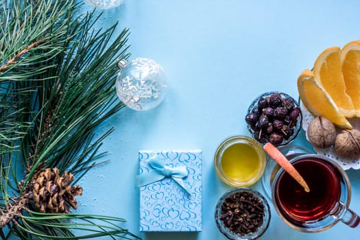 Hot mulled wine with orange, anise, cardamon and cinnamon on blue background. Christmas tree branches, gifts and cones. Flat lay, copy space, top view. Holidays.
