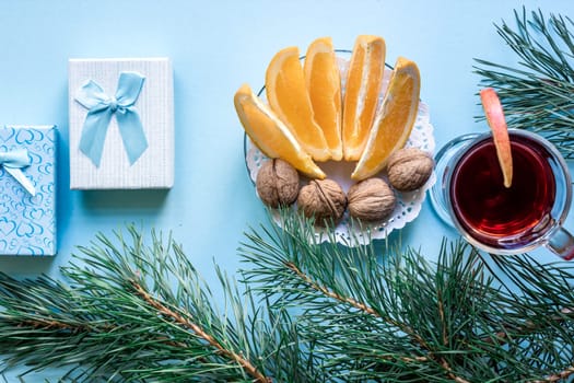 Hot mulled wine with orange, anise, cardamon and cinnamon on blue background. Christmas tree branches, gifts and cones. Flat lay, copy space, top view. Holidays.