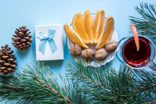 Hot mulled wine with orange, anise, cardamon and cinnamon on blue background. Christmas tree branches, gifts and cones. Flat lay, copy space, top view. Holidays.