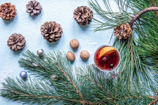 Hot mulled wine with orange, anise, cardamon and cinnamon on blue background. Christmas tree branches, gifts and cones. Flat lay, copy space, top view. Holidays.
