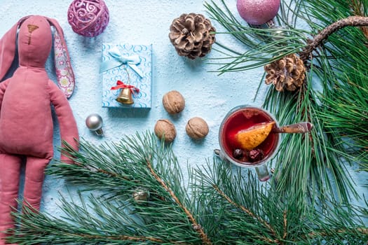 Hot mulled wine with orange, anise, cardamon and cinnamon on blue background. Christmas tree branches, gifts and cones. Flat lay, copy space, top view. Holidays.