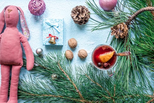 Hot mulled wine with orange, anise, cardamon and cinnamon on blue background. Christmas tree branches, gifts and cones. Flat lay, copy space, top view. Holidays.