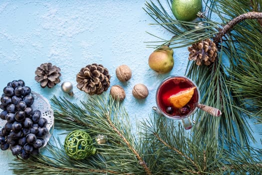 Hot mulled wine with orange, anise, cardamon and cinnamon on blue background. Christmas tree branches, gifts and cones. Flat lay, copy space, top view. Holidays.