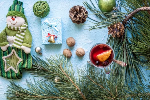 Hot mulled wine with orange, anise, cardamon and cinnamon on blue background. Christmas tree branches, gifts and cones. Flat lay, copy space, top view. Holidays.