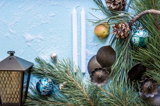 Christmas decoration. Branch christmas tree and cones spruce, antique candlesticks, candles, glass balls on snow on blue background. Top view, flat lay