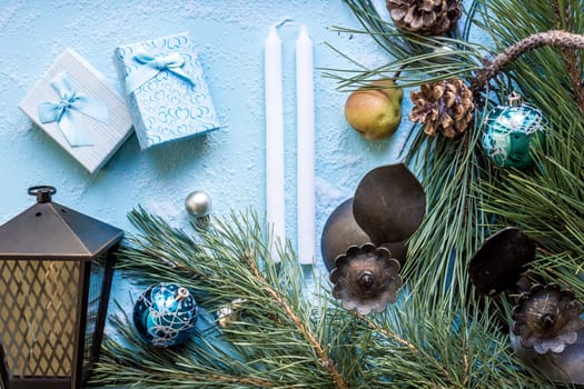 Christmas decoration. Branch christmas tree and cones spruce, antique candlesticks, candles, glass balls on snow on blue background. Top view, flat lay