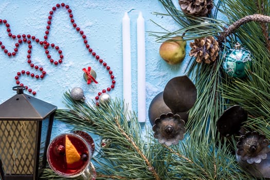 Hot mulled wine with orange, anise, cardamon and cinnamon on blue background. Christmas tree branches, gifts and cones. Flat lay, copy space, top view. Holidays.