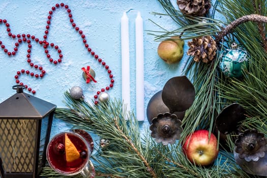 Hot mulled wine with orange, anise, cardamon and cinnamon on blue background. Christmas tree branches, gifts and cones. Flat lay, copy space, top view. Holidays.