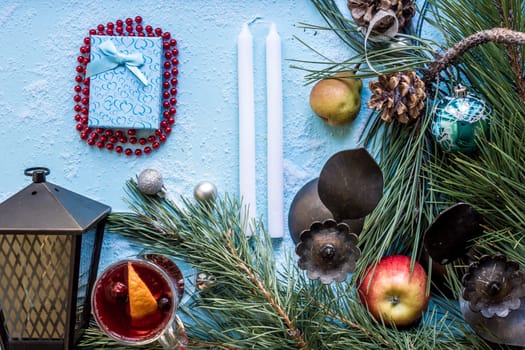 Hot mulled wine with orange, anise, cardamon and cinnamon on blue background. Christmas tree branches, gifts and cones. Flat lay, copy space, top view. Holidays.