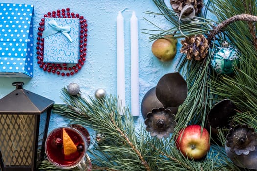 Hot mulled wine with orange, anise, cardamon and cinnamon on blue background. Christmas tree branches, gifts and cones. Flat lay, copy space, top view. Holidays.