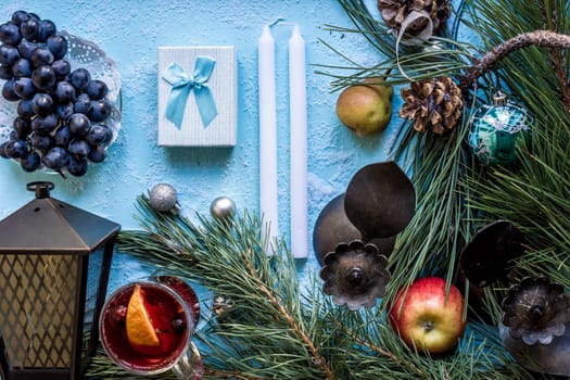 Hot mulled wine with orange, anise, cardamon and cinnamon on blue background. Christmas tree branches, gifts and cones. Flat lay, copy space, top view. Holidays.