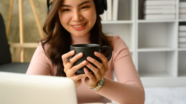 Pretty young woman looking at laptop screen and drinking hot beverage in morning. People and lifestyle concept.