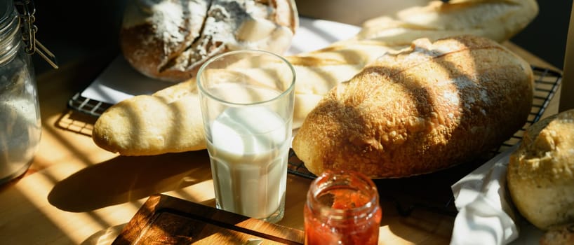 A glass of milk and baked bread on table in kitchen with sunlight from window.