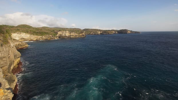 Rocky coast with high cliffs, sea surf with breaking waves on the coast, Nusa Penida, Indonesia. Ocean with waves and rocky cliff. Travel concept.