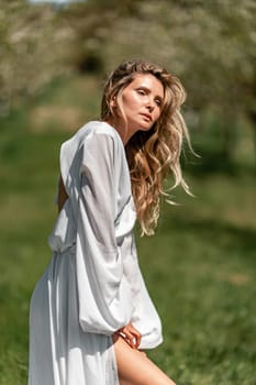 Blond blooming garden. A woman in a white dress walks through a blossoming cherry orchard. Long dress flies to the sides