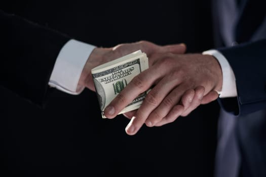 Handshake with the transfer of money on a black background