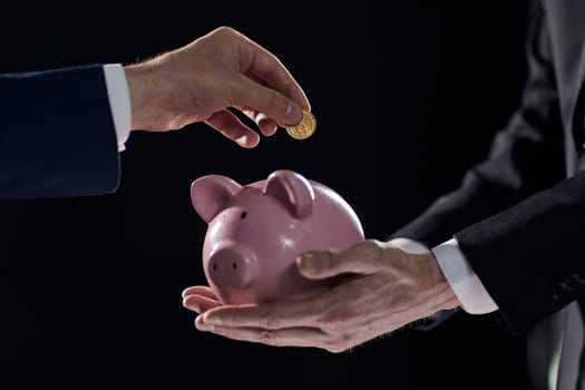 Hand puts a coin in a piggy bank on a black background. accumulation concept