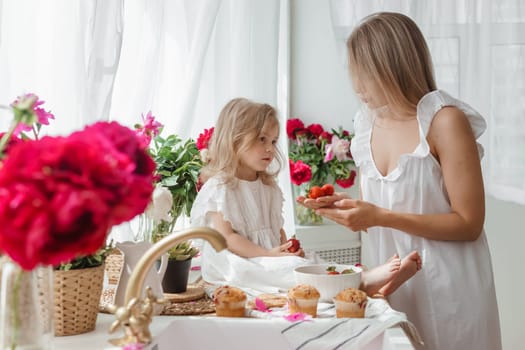 A little blonde girl with her mom on a kitchen countertop decorated with peonies. The concept of the relationship between mother and daughter. Spring atmosphere