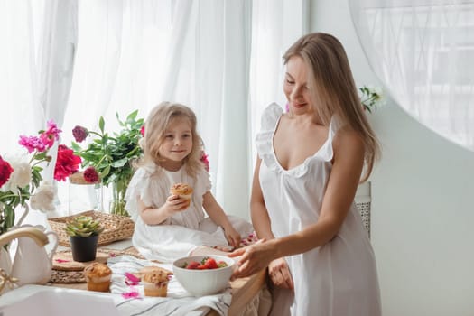 A little blonde girl with her mom on a kitchen countertop decorated with peonies. The concept of the relationship between mother and daughter. Spring atmosphere