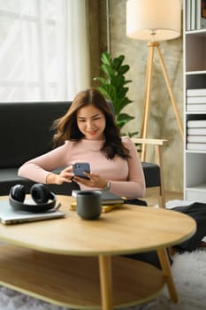 Attractive asian woman using smartphone in cozy living room. Technology and communicating concept.