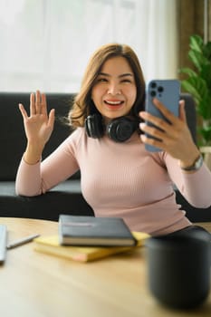 Smiling millennial woman waving hand, making video calling on smartphone. People, technology and communicating.