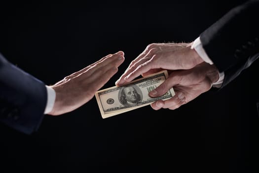 A man's hand in a black suit holds out a wad of money, which refuses. On a black background