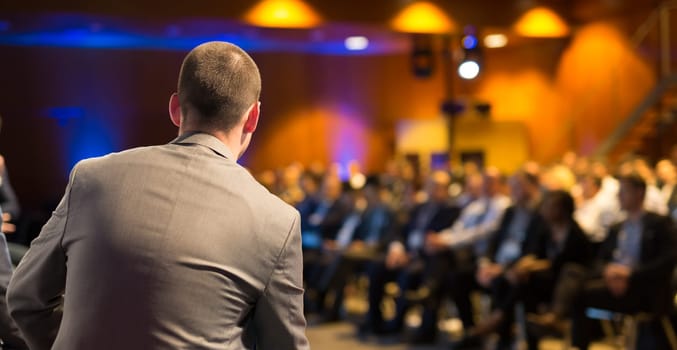 Speaker giving a talk on corporate business conference. Unrecognizable people in audience at conference hall. Business and Entrepreneurship event.