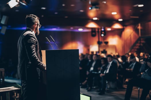 Speaker giving a talk on corporate business conference. Unrecognizable people in audience at conference hall. Business and Entrepreneurship event.