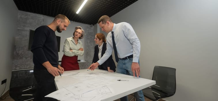 Four business people review and discuss blueprints. Designers engineers at a meeting