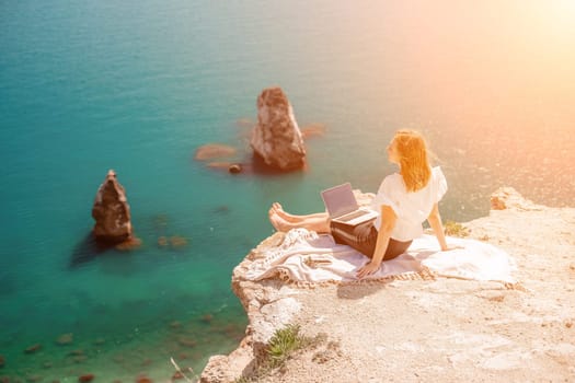 Freelance woman working on a laptop by the sea, typing away on the keyboard while enjoying the beautiful view, highlighting the idea of remote work