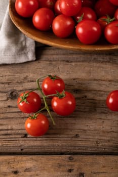 Directly above view of fresh red cherry tomatoes with plate and napkin on wooden table. unaltered, organic food and healthy eating concept.