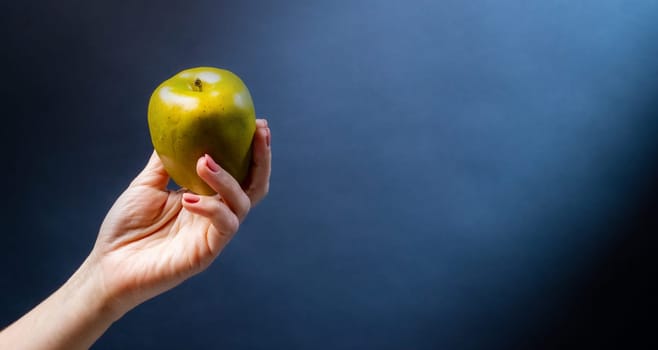 Hand holding green apple on blue background. Organic natural fresh fruit for vegan diet