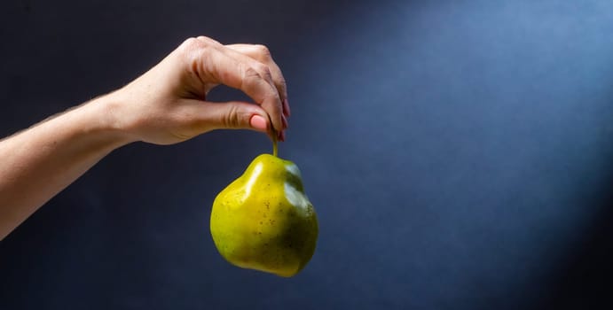 Hand holding green pear on blue background. Organic natural fresh fruit for healthy vitamin vegan diet