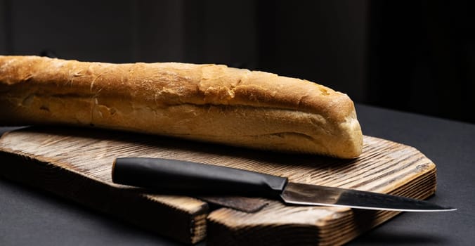 French baguette for bruschettas on wooden board with knife with copy space. Rustic crusty bread loaf for teraditional snacks