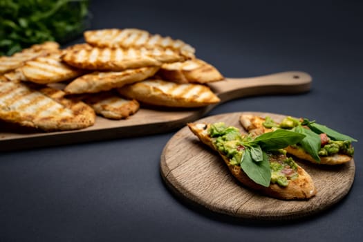 Bruschettas with toast, guacamole, basil and cherry tomatoes on wooden board. Mexican snack slice bread with avocado, herbs and vegetables