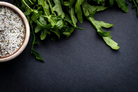 Green arugula and salt with herbs on dark grey background with copy space. Healthy food composition of organic vegan nutrition