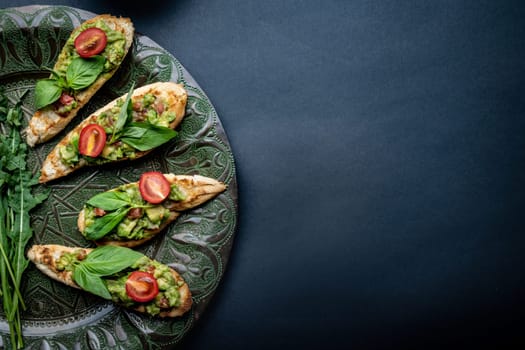 Bruschettas french toasts with guacamole, basil and cherry tomatoes served on beautiful plate with arugula. Antipasti with slice bread, mashed avocado and vegetables on background with copy space