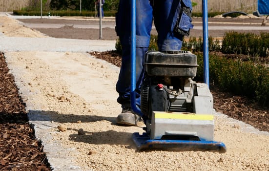 Legs and feet of a man who operates a sand compactor. The man is vibrating the sand of a new path.