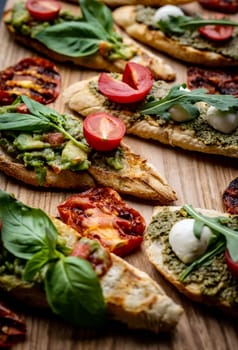 Set of bruschettas with pesto, guacamole, grilled tomatoes, mozzarella cheese, basil and arugula on wooden board. Italian tosted bread with vegetables and traditional sauces