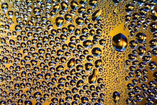 glass covered with drops of water. water drops on yellow background texture.