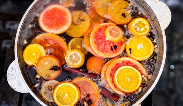 Mulled spicy vine with oranges in pot in street food market. Colorful hot alcohol drink at fair festival outdoors closeup